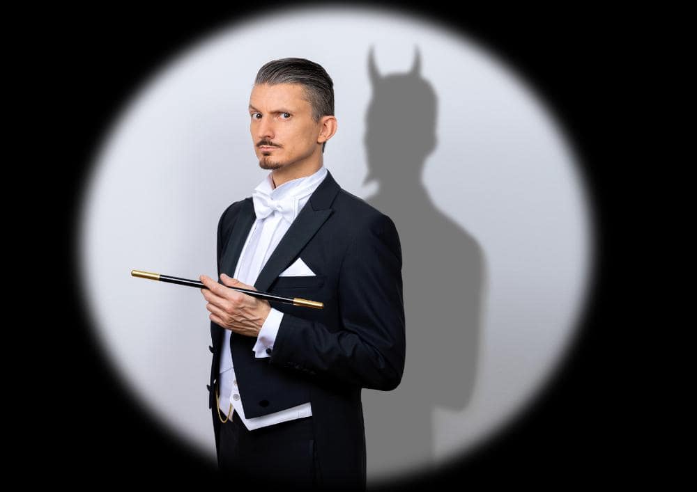 Wolfgang Moser ist Zauberkünstler. Abgebildet vor einem weissen Kreis an einer schwarzen Wand. Als Schatten sieht man von ihm den Teufel